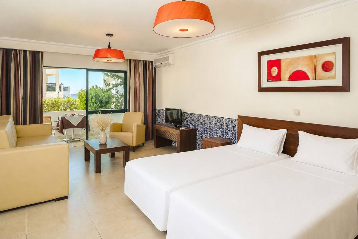 A hotel room with a bed, a sofa, a coffee table, a TV, and a painting on the wall.