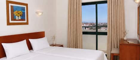 Een hotelkamer met een bed, een bureau, een stoel, een raam met gordijnen, een vaas met bloemen en een ingelijst schilderij aan de muur.