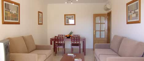 A living room with a sofa, a coffee table, a dining table with chairs, and framed pictures on the walls.