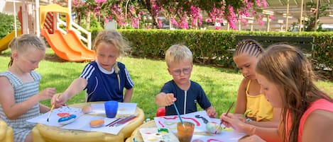 A group of children painting outdoors with a playground in the background.