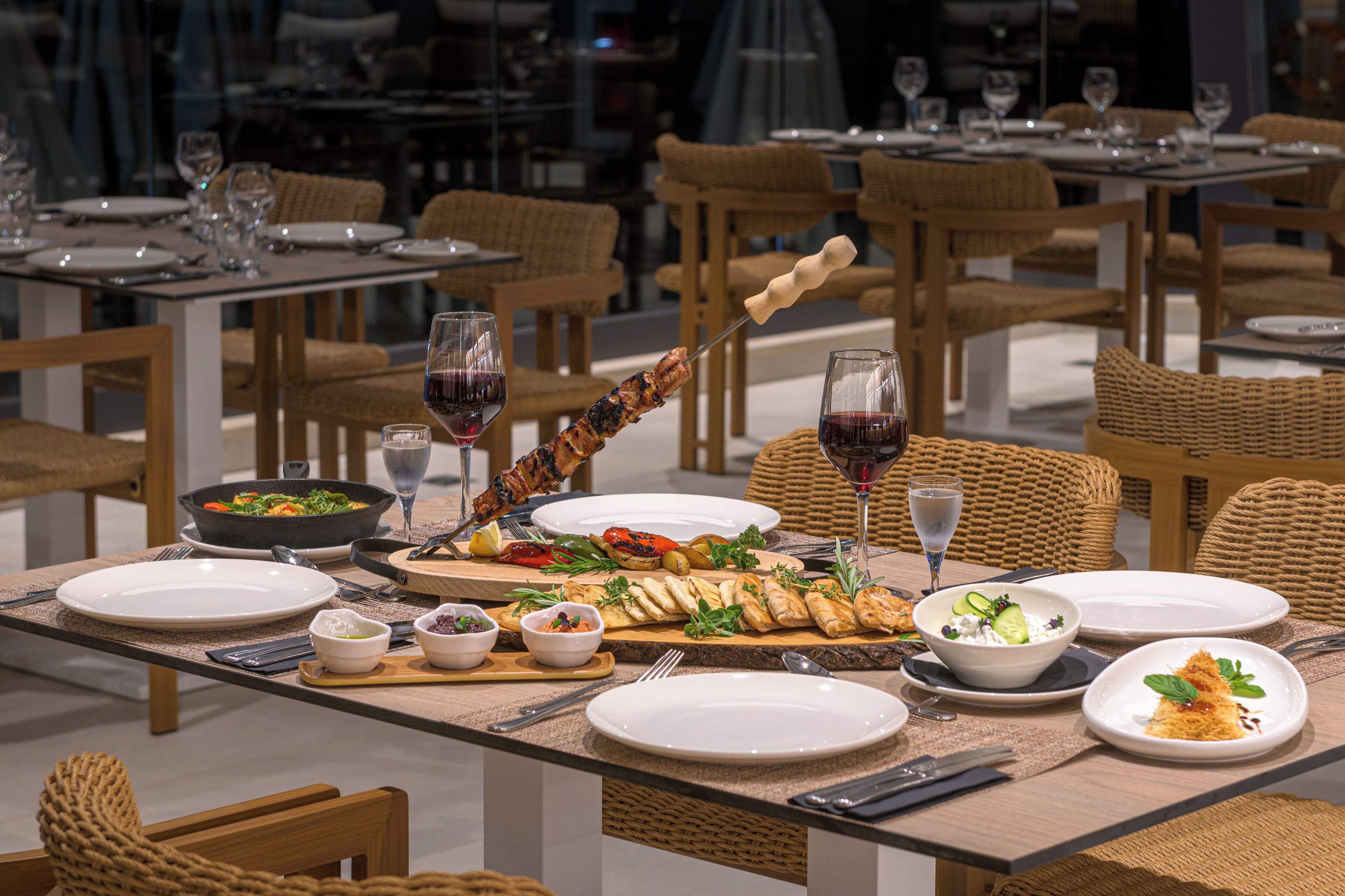 A dining table set with plates, cutlery, a bowl of salad, a skewer of food, and a glass of red wine.