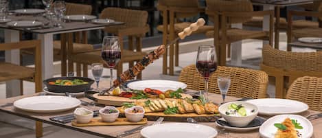A dining table set with plates, cutlery, a bowl of salad, a skewer of food, and a glass of red wine.