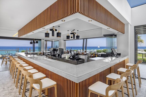 Un bar moderno con un revestimiento de madera, taburetes y vista al océano.