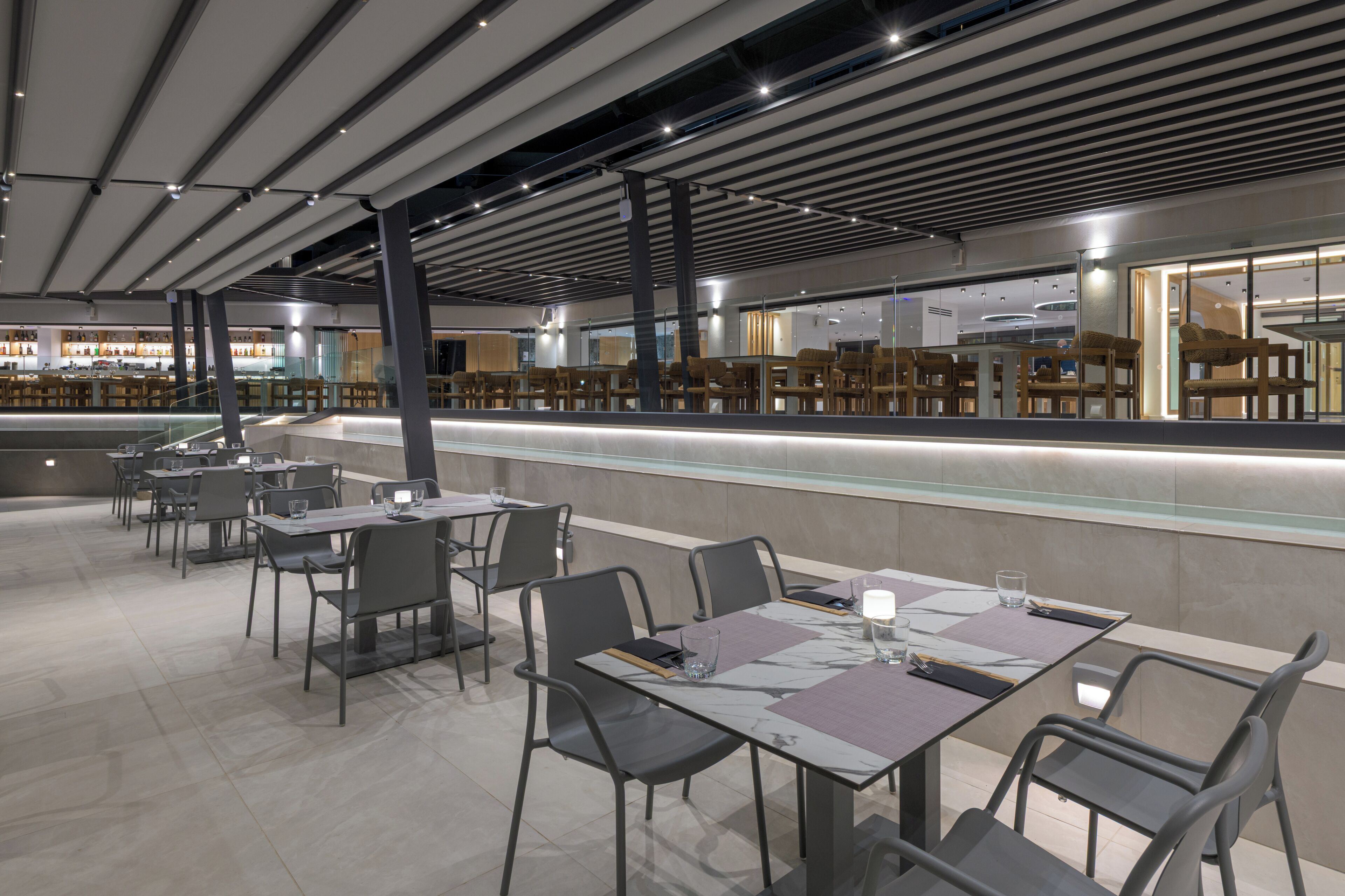 A modern restaurant with a long counter, multiple tables, and chairs.