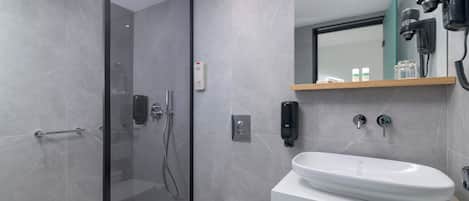 A modern bathroom with a glass shower enclosure, a white toilet, a sink with a mirror above, and a hairdryer mounted on the wall.