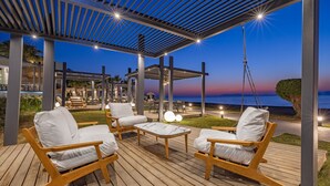 Une terrasse extérieure avec des meubles en bois et une pergola, donnant sur un plan d’eau.