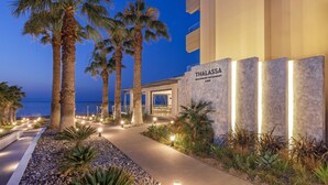 Un restaurant en bord de mer appelé Thalassa, avec un chemin bordé de palmiers et une vue sur la mer.