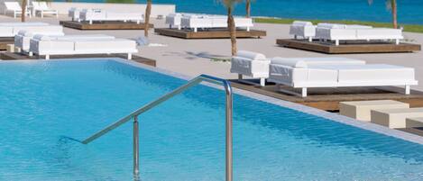 A pool area with lounge chairs and a view of the ocean.