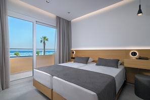A modern hotel room with a large bed, a bedside table, a nightstand, and a view of the beach. - Sun Beach Resort (Rhodes)