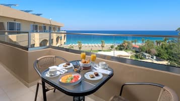 Un balcón con una mesa dispuesta para el desayuno, con vista a una playa y al océano.