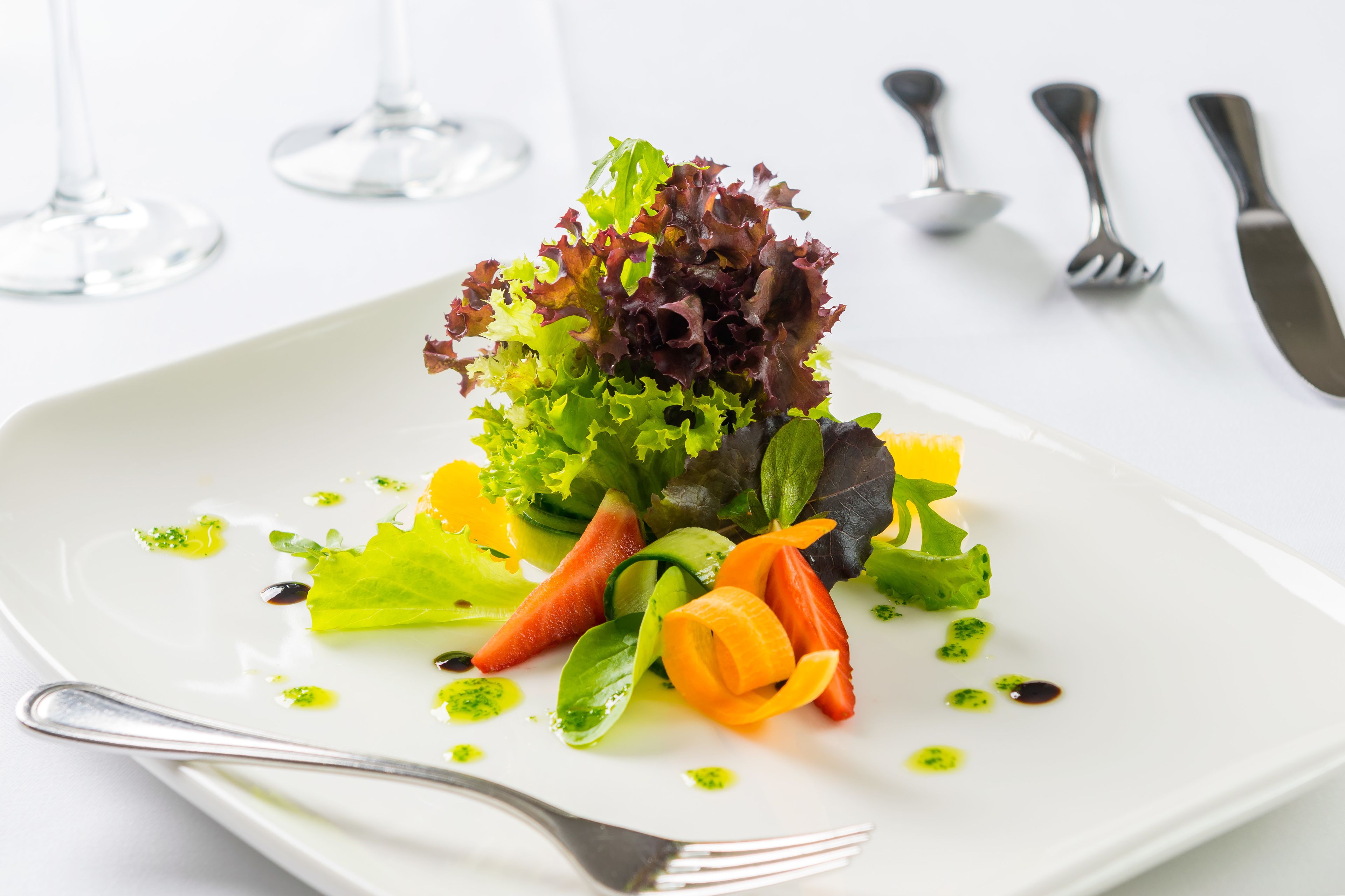 A white plate with a salad, a fork, and a knife on a table.