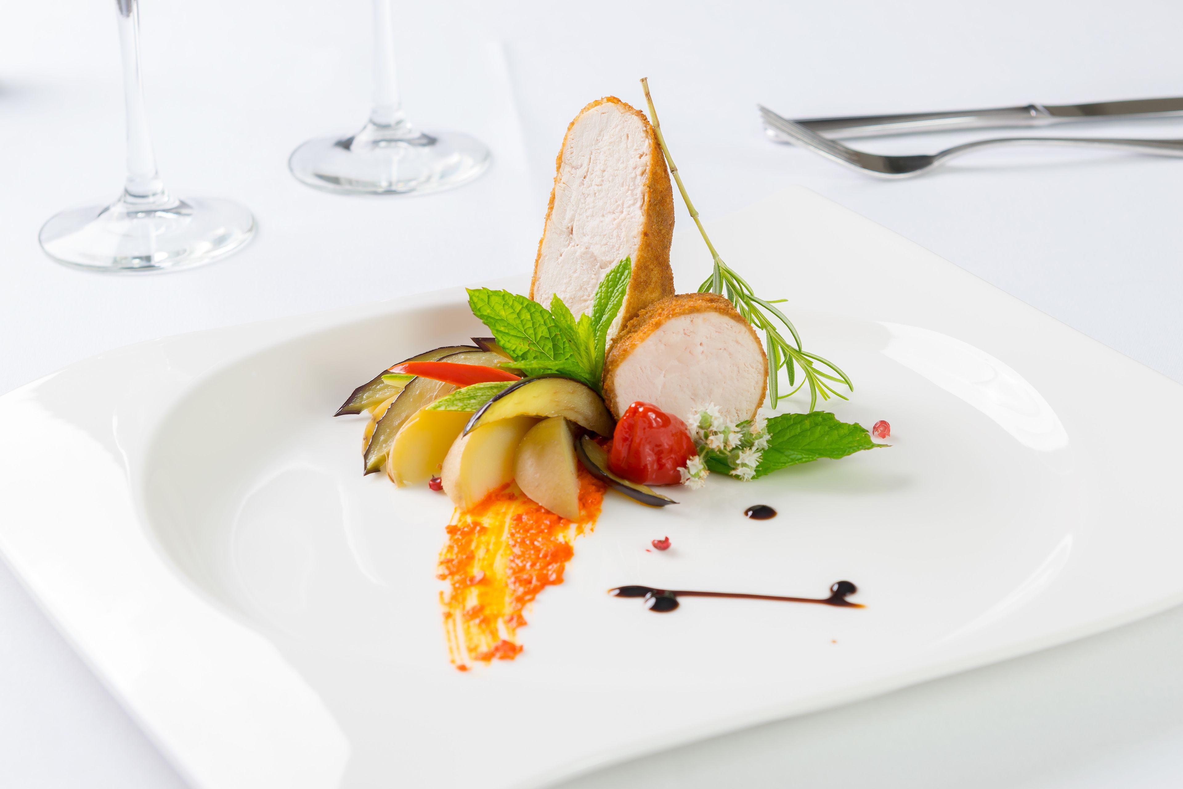 Een wit bord met een etouffée, inclusief plakjes vlees, groenten en garnering, op een witte tafelkleed.