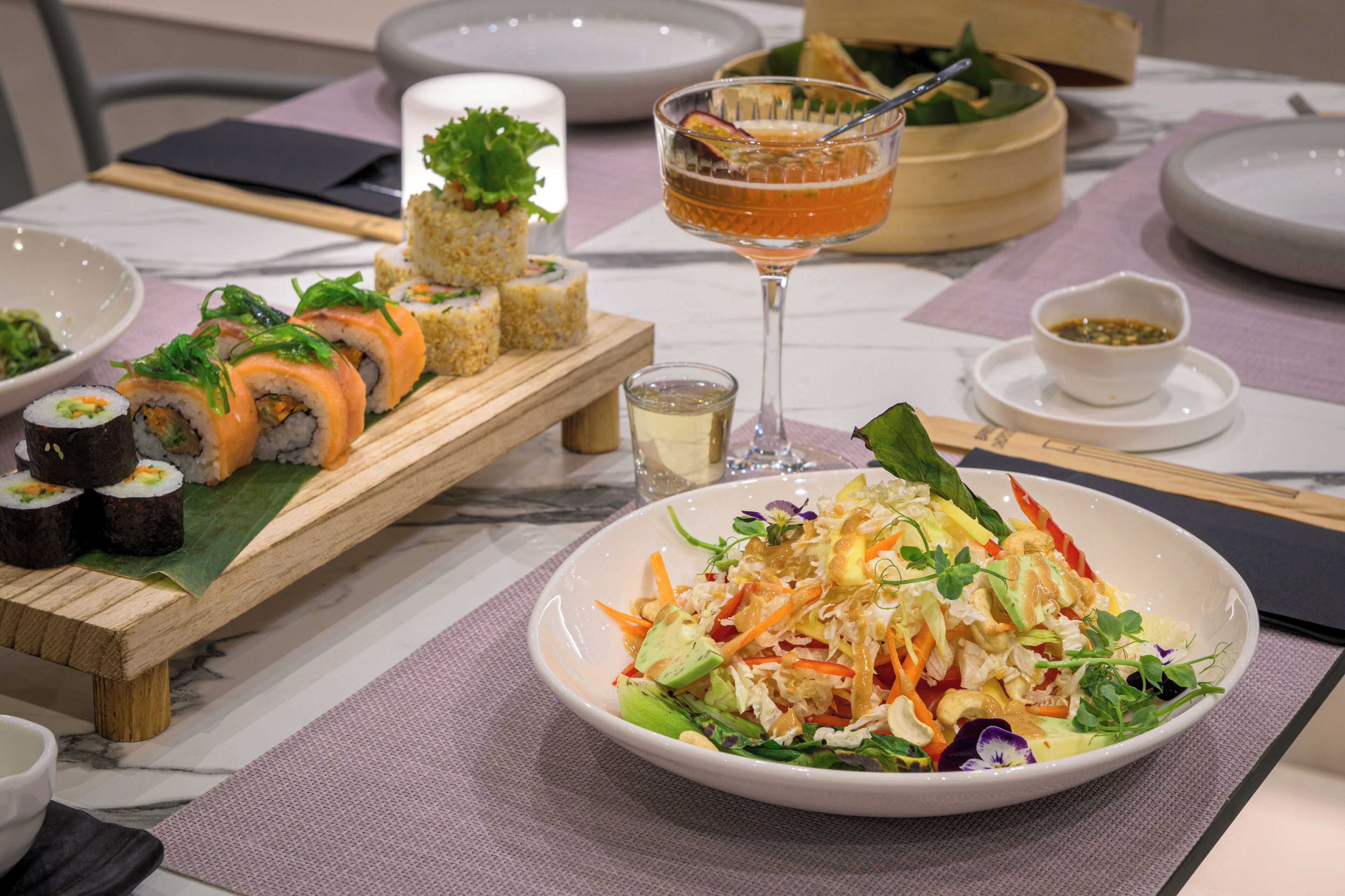 Une table à manger avec des sushis, une salade, une boisson et un petit bol de sauce.