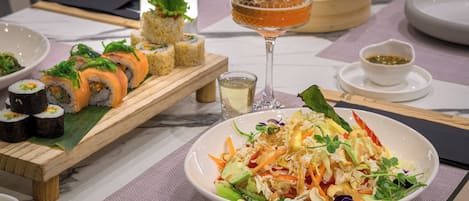 Ett matbord med sushi, en sallad, en drink och en liten skål med sås.