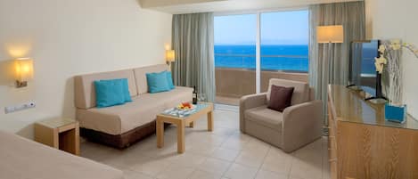 Habitación de hotel con balcón, sofá, sillón, mesita de centro y televisor.