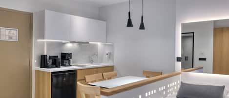 A compact kitchen with a dishwasher, coffee maker, and a dining area with a wooden table and chairs.