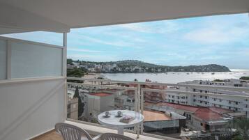 A balcony with a table and chairs, overlooking a beach and a commercial area with buildings and shops.