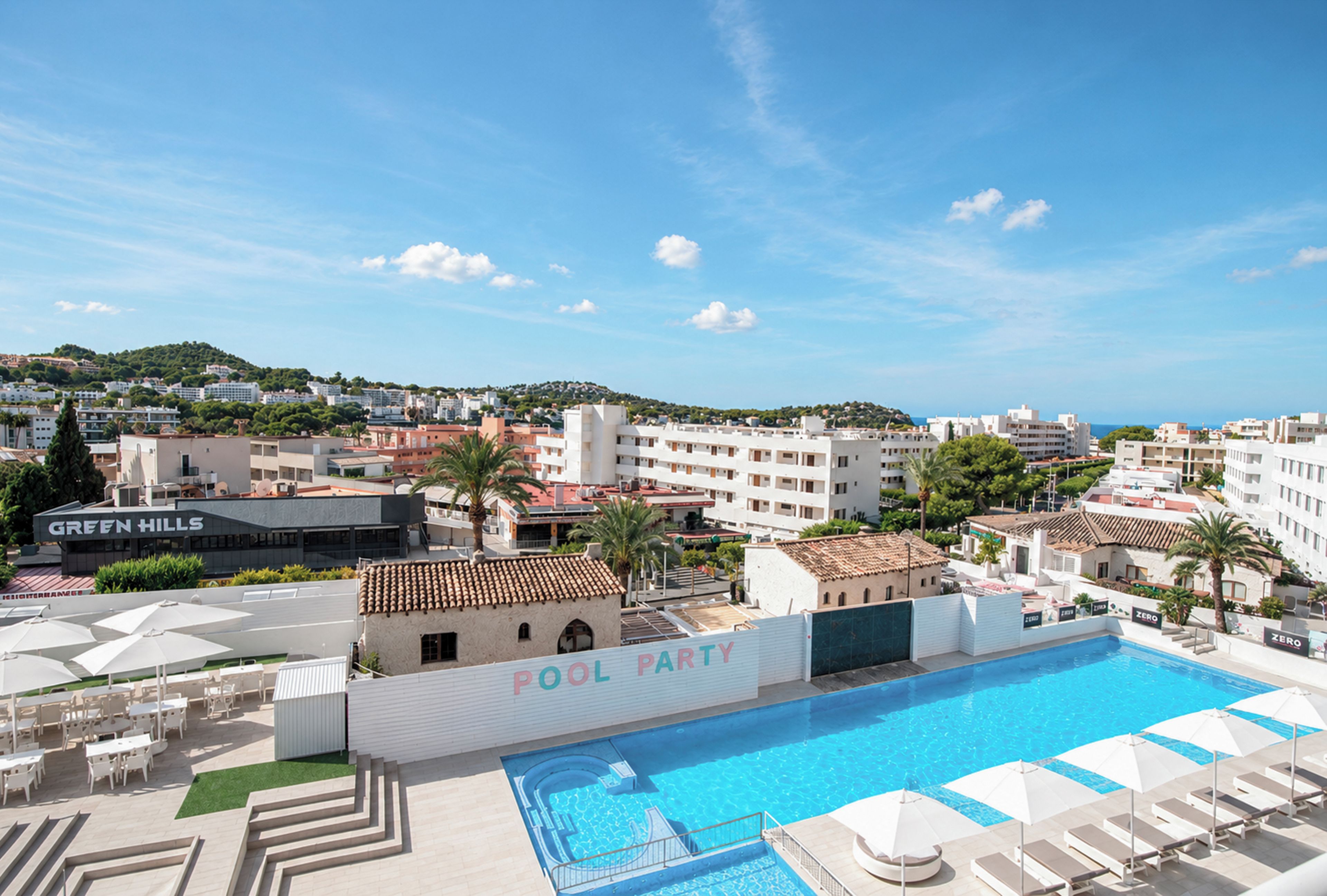 A rooftop pool area with lounge chairs and umbrellas, a pool, and a view of the cityscape in the background.