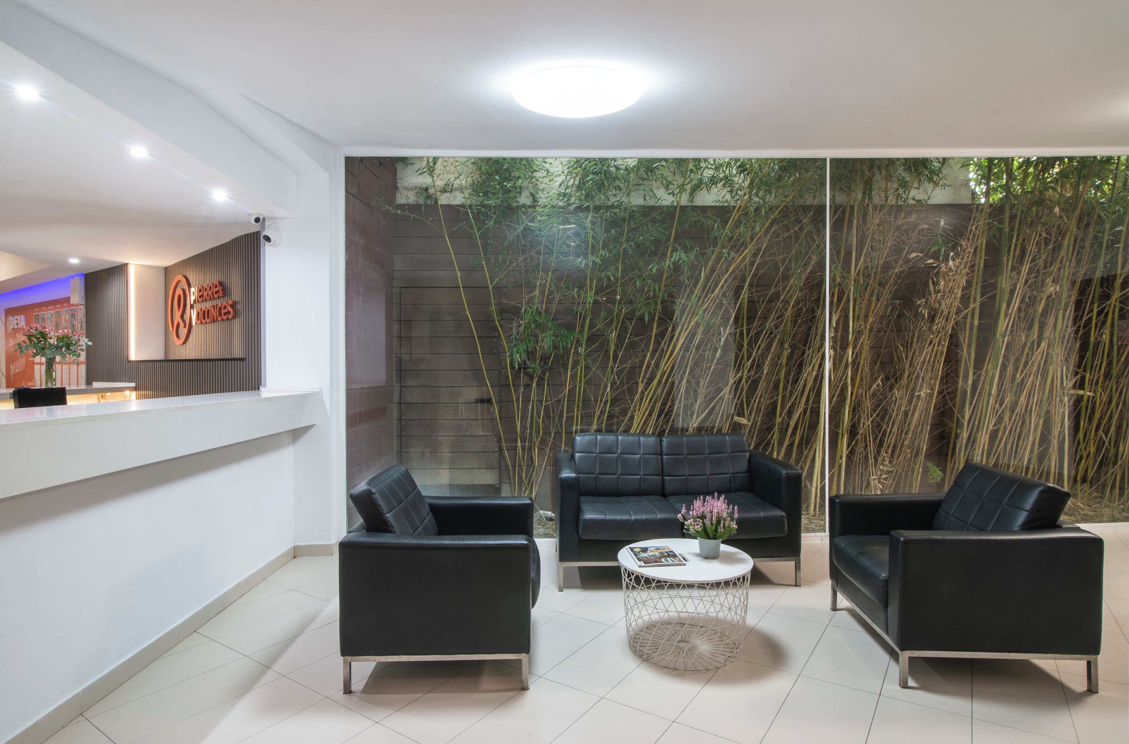 A modern interior with a reception desk, black leather sofas, a round coffee table, and a bamboo backdrop.