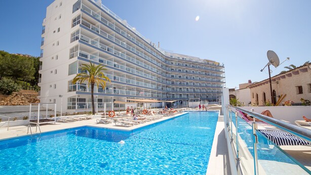 Un hotel moderno con piscina, varios balcones y un cielo despejado.