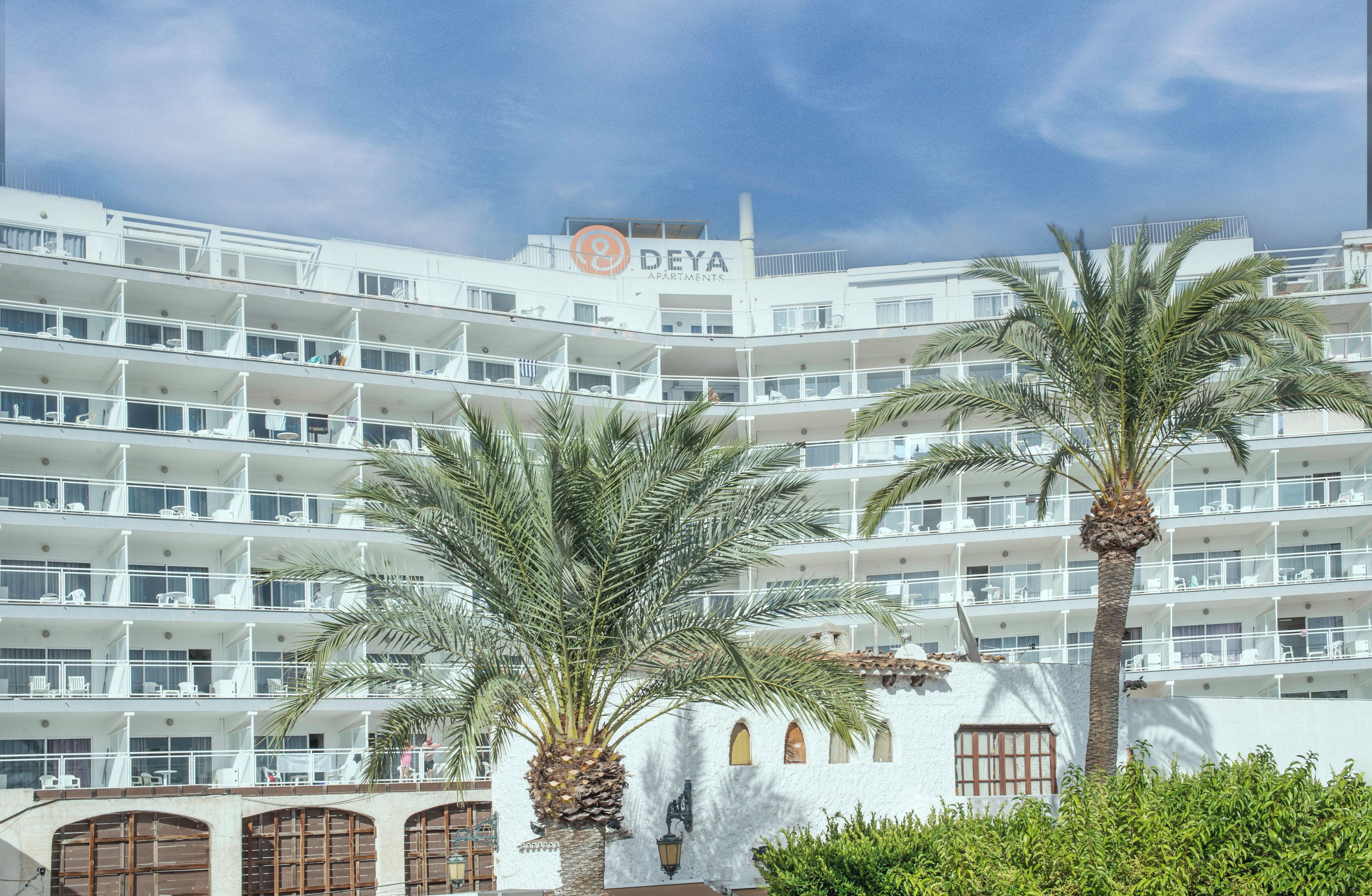 Et hotel med flere etager, altaner, palmer og en klar himmel.