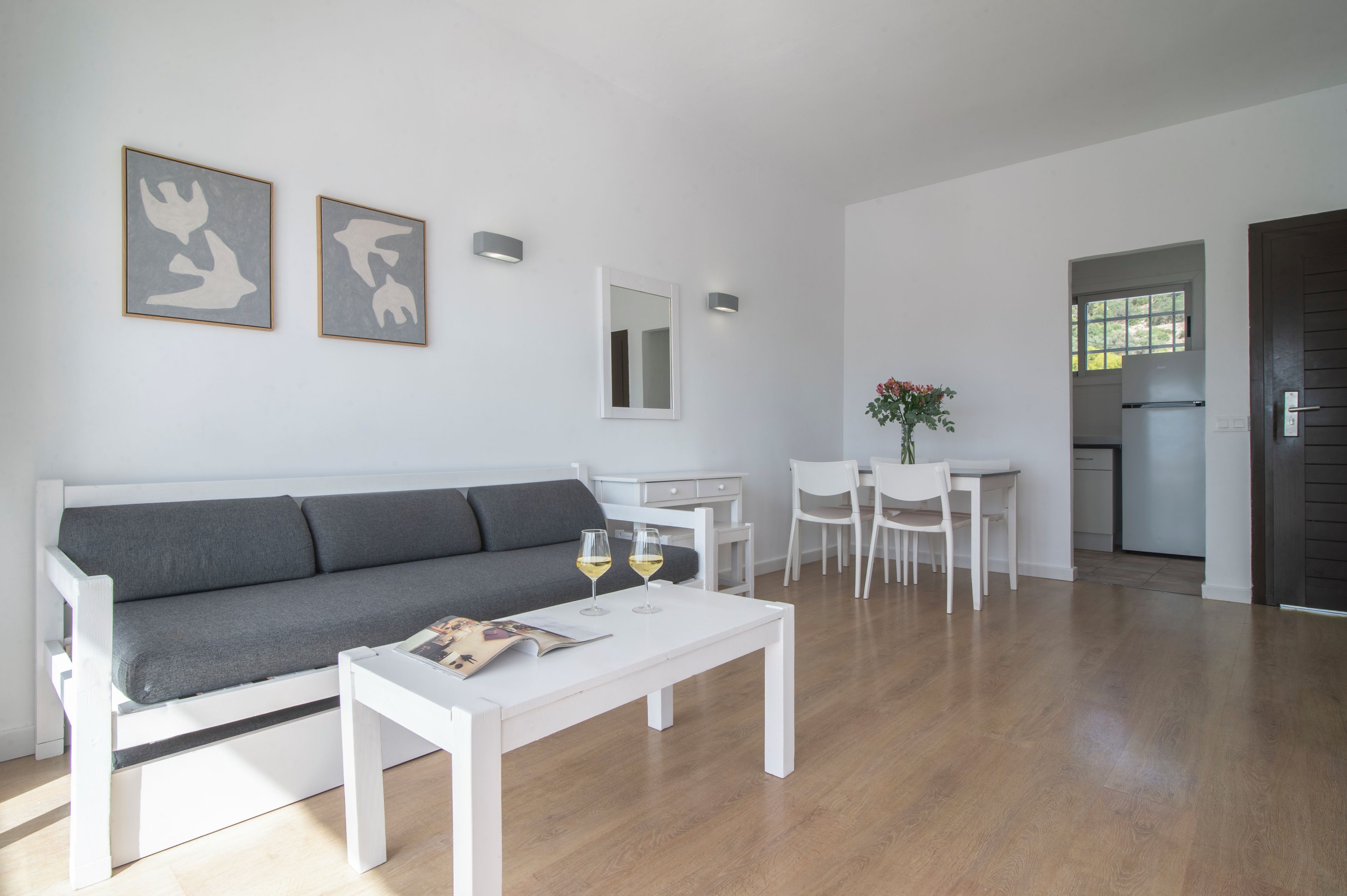 Una sala moderna con un sofá gris, una mesita de centro blanca y dos copas de vino.