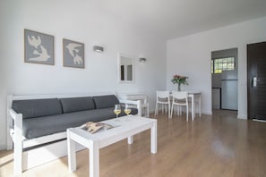 A modern living room with a grey sofa, white coffee table, and two wine glasses. - Pierre & Vacances Mallorca Deya - Recomendado para adultos (Calvia)