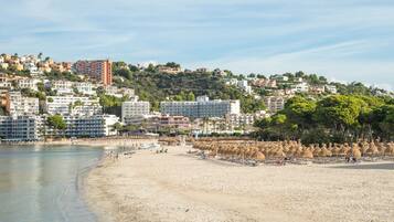 A coastal cityscape with a sandy beach, buildings, and a hilly backdrop.