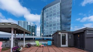Terraza en la azotea con mobiliario exterior, una parrilla y vistas a edificios modernos.
