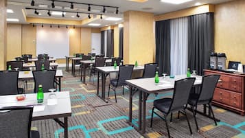 A hotel conference room with multiple tables, chairs, and a projection screen.