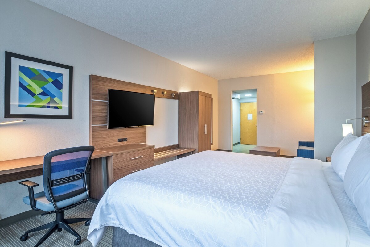 A hotel room with a large bed, a desk with a chair, a flat-screen TV, and a framed abstract painting on the wall.