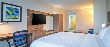 A hotel room with a bed, a desk with a chair, a flat-screen TV, and a framed picture on the wall.