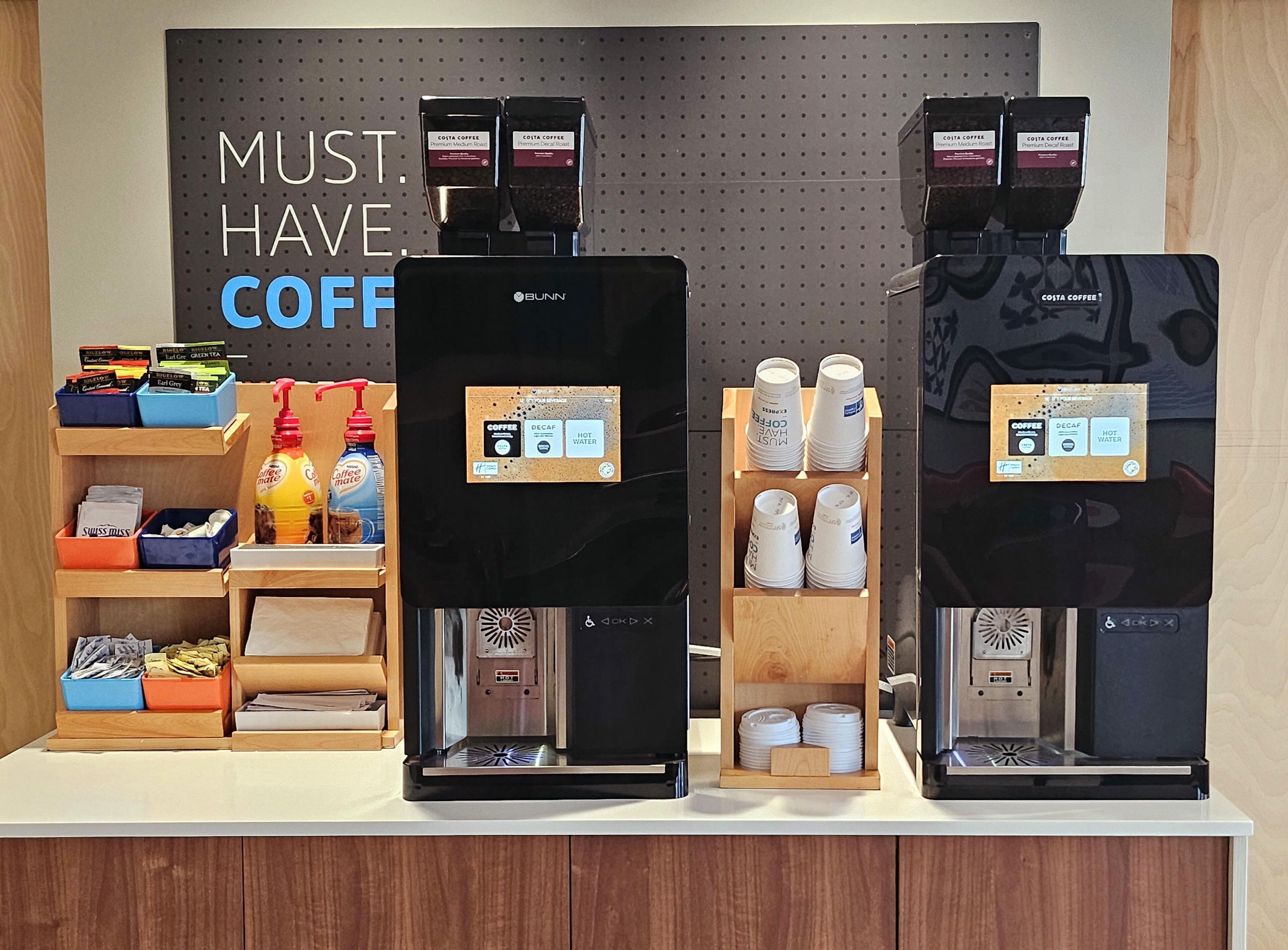 Una estación de café con dos máquinas de café, un dispensador y un cartel que dice "MUST HAVE COFFEE".