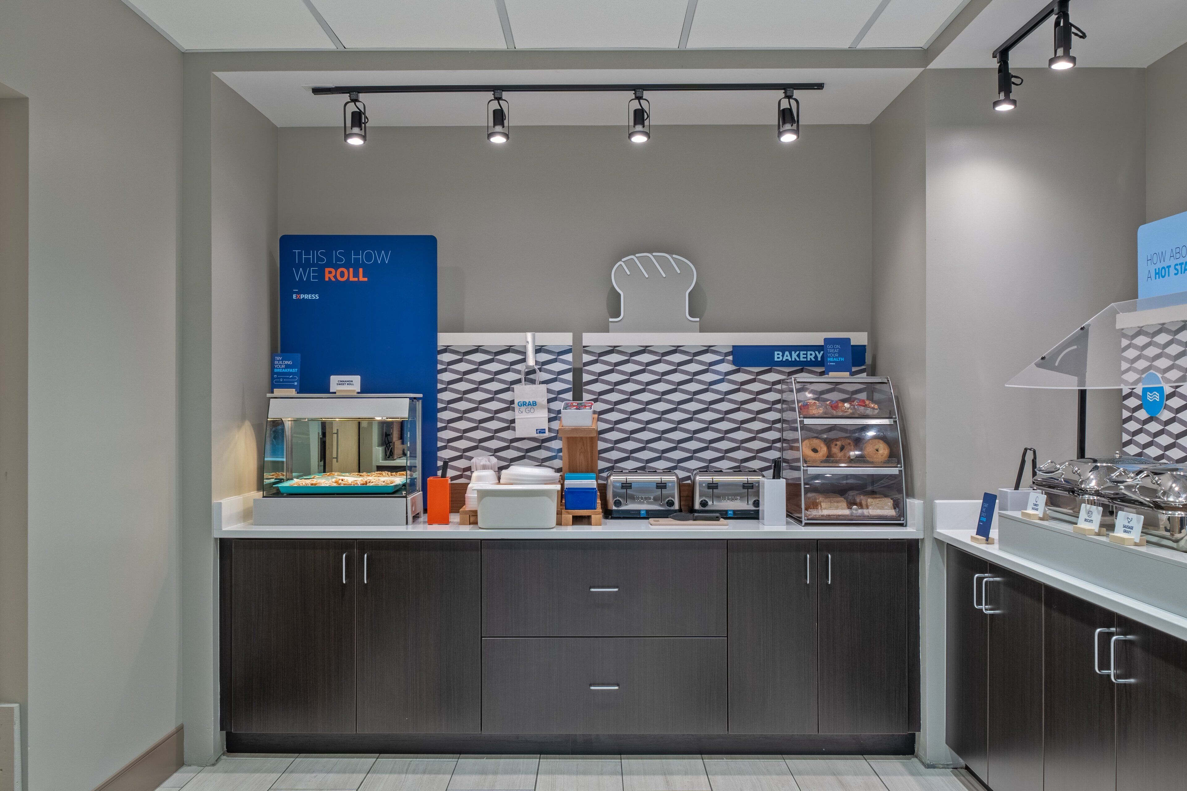 A modern kitchen with a counter displaying various food items and a sign that says "THIS IS HOW WE ROLL".