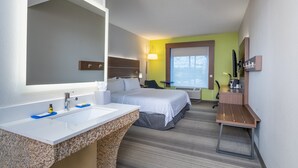 Habitación de hotel con un espejo grande, un lavamanos blanco, dos camas, un escritorio y una silla.
