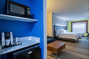 A hotel room with a kitchenette, a bed, a desk, and a window with a view.