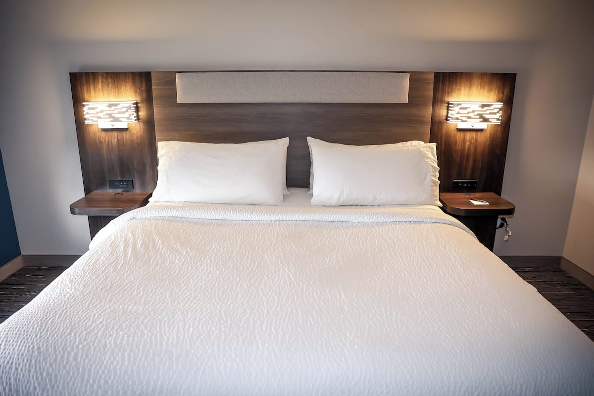 Una cama bien hecha con sábanas blancas, dos mesitas de noche con apliques de luz, y un cabecero de madera.