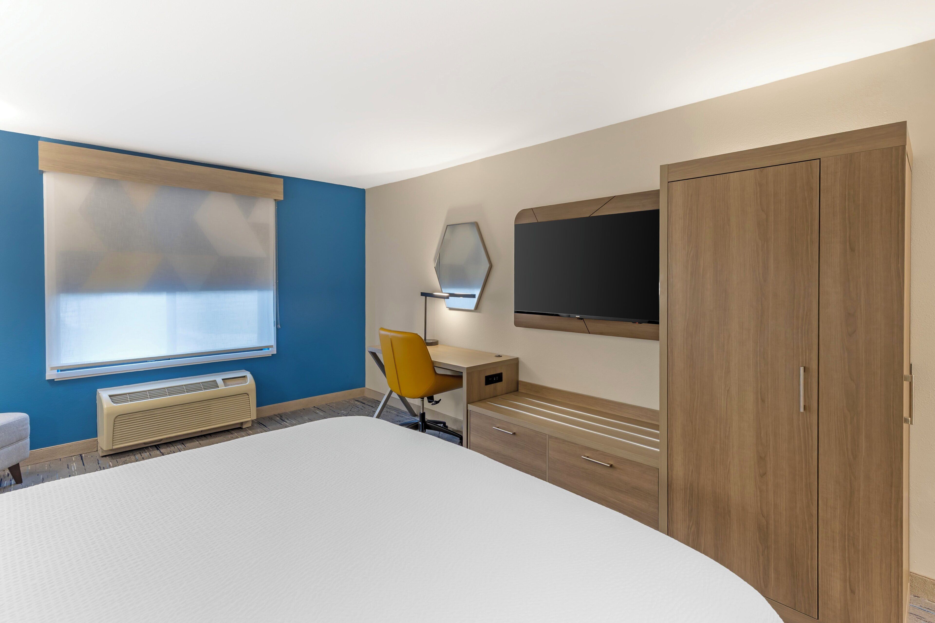 A hotel room with a bed, a desk, a chair, a wardrobe, and a television.