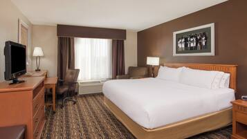 A hotel room with a large bed, a desk with a computer, a chair, a television, and a window with curtains.