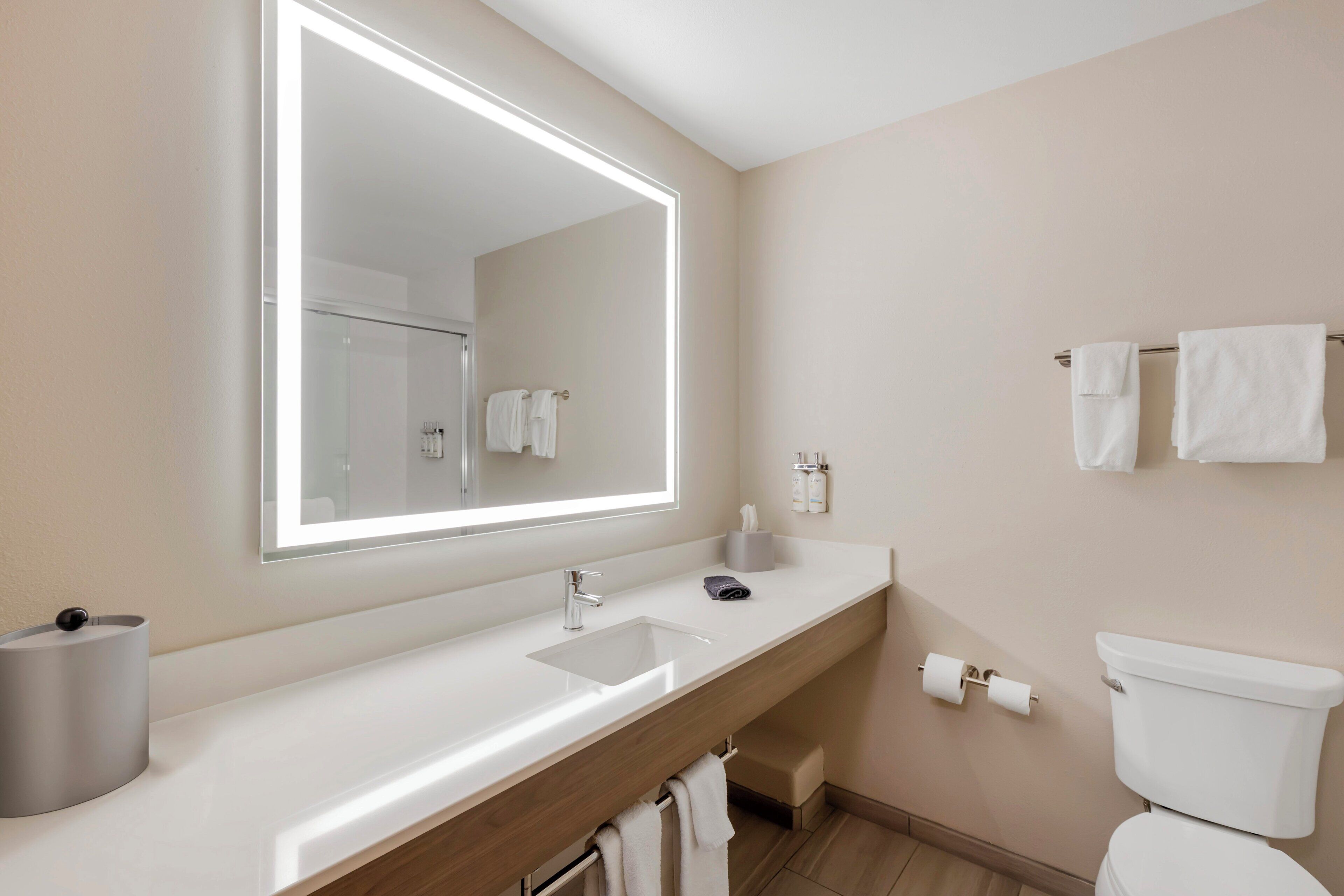 A modern bathroom with a large mirror, a sink, a toilet, and a towel rack.
