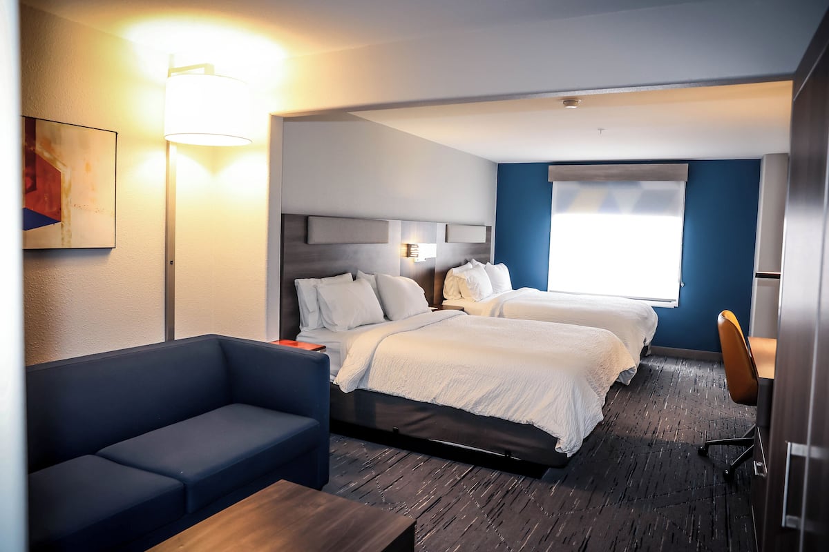 Una habitación de hotel con dos camas, un sofá, un escritorio y una lámpara.