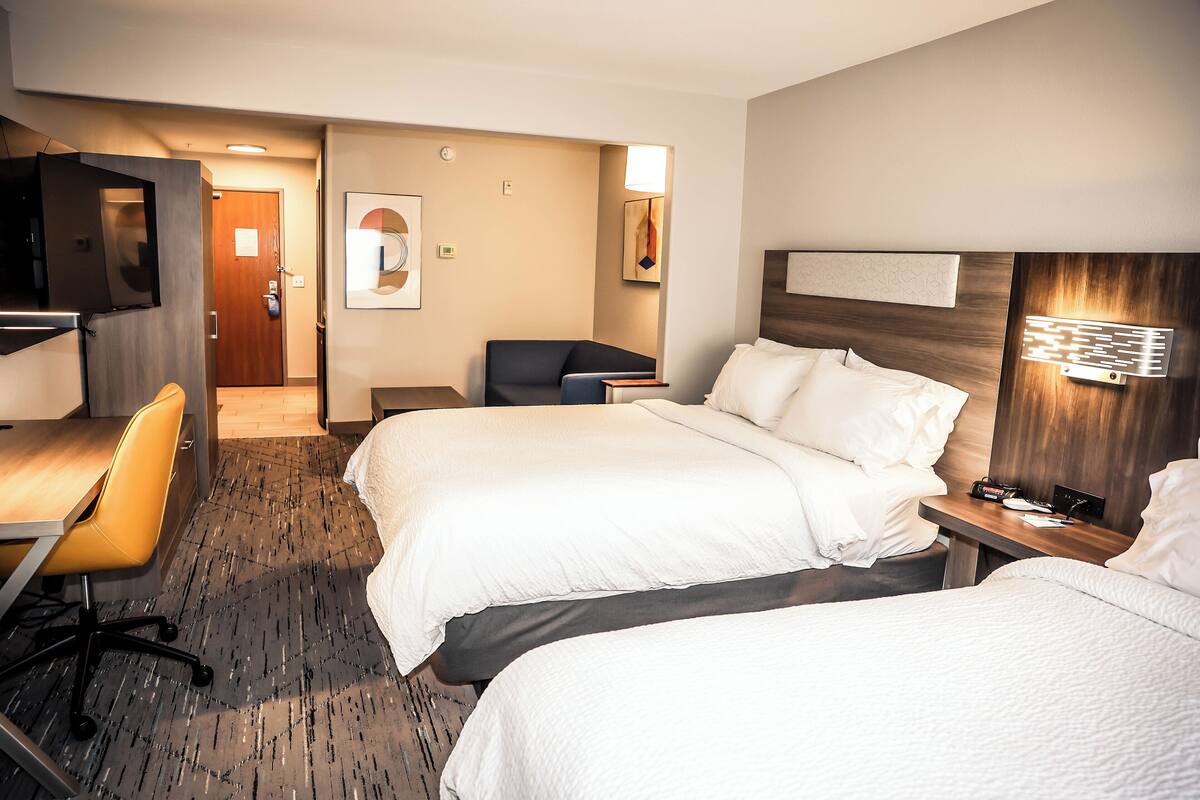 Habitación de hotel con dos camas, un escritorio, una silla y un televisor.