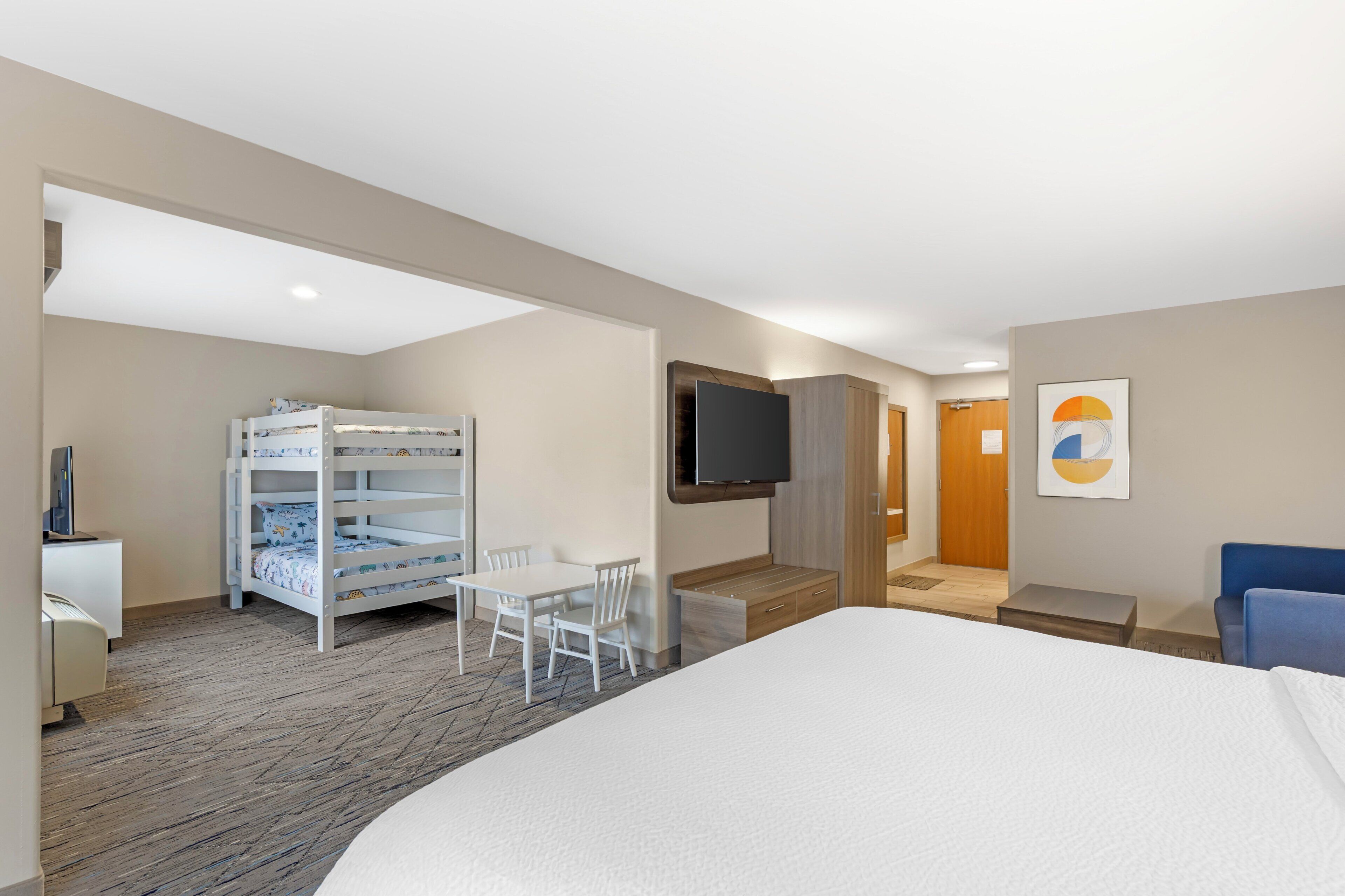 A hotel room with a bed, a desk, a TV, a bunk bed, and a chair.