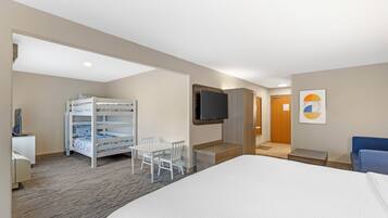 A hotel room with a bed, a desk, a TV, a bunk bed, and a chair.
