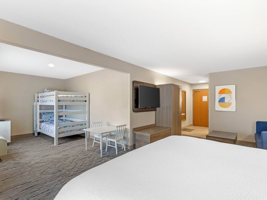 A hotel room with a bed, a desk, a TV, a bunk bed, and a chair.