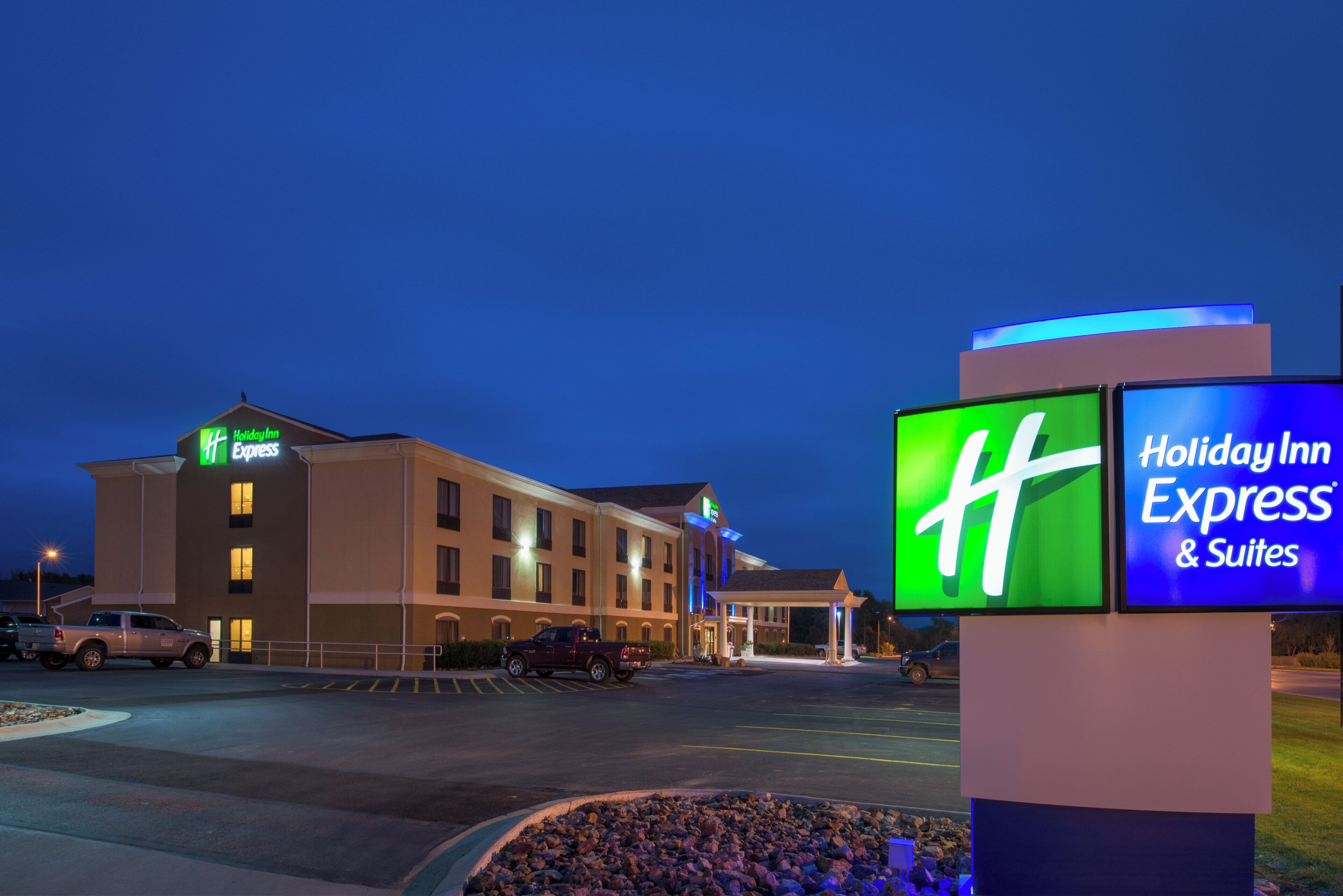 Ein Holiday Inn Express & Suites Hotel mit einer großen beleuchteten Signatur, einem Parkplatz und einem Gebäude mit zahlreichen Fenstern.