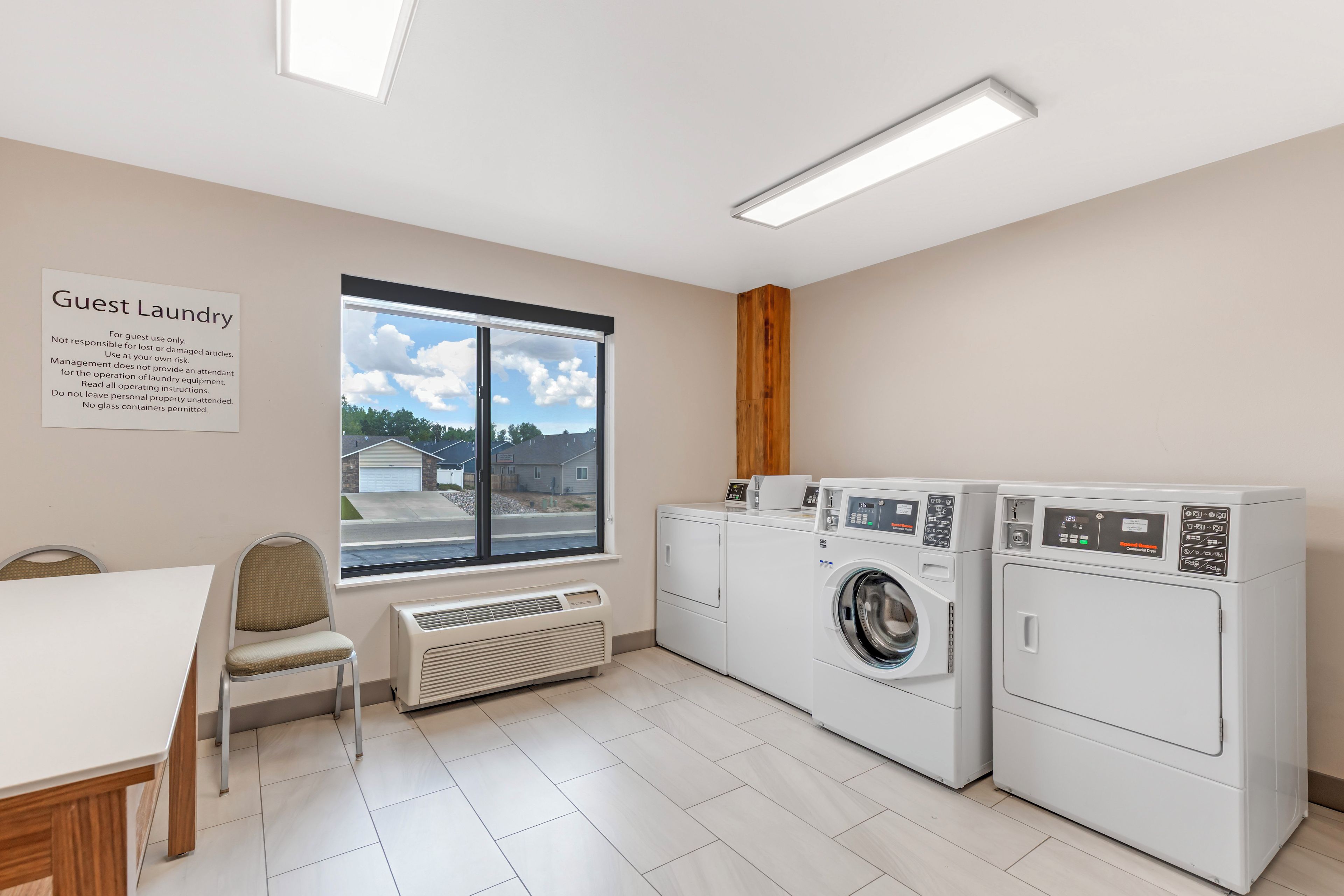 A guest laundry area with a sign, a chair, a table, a window, and two washing machines.