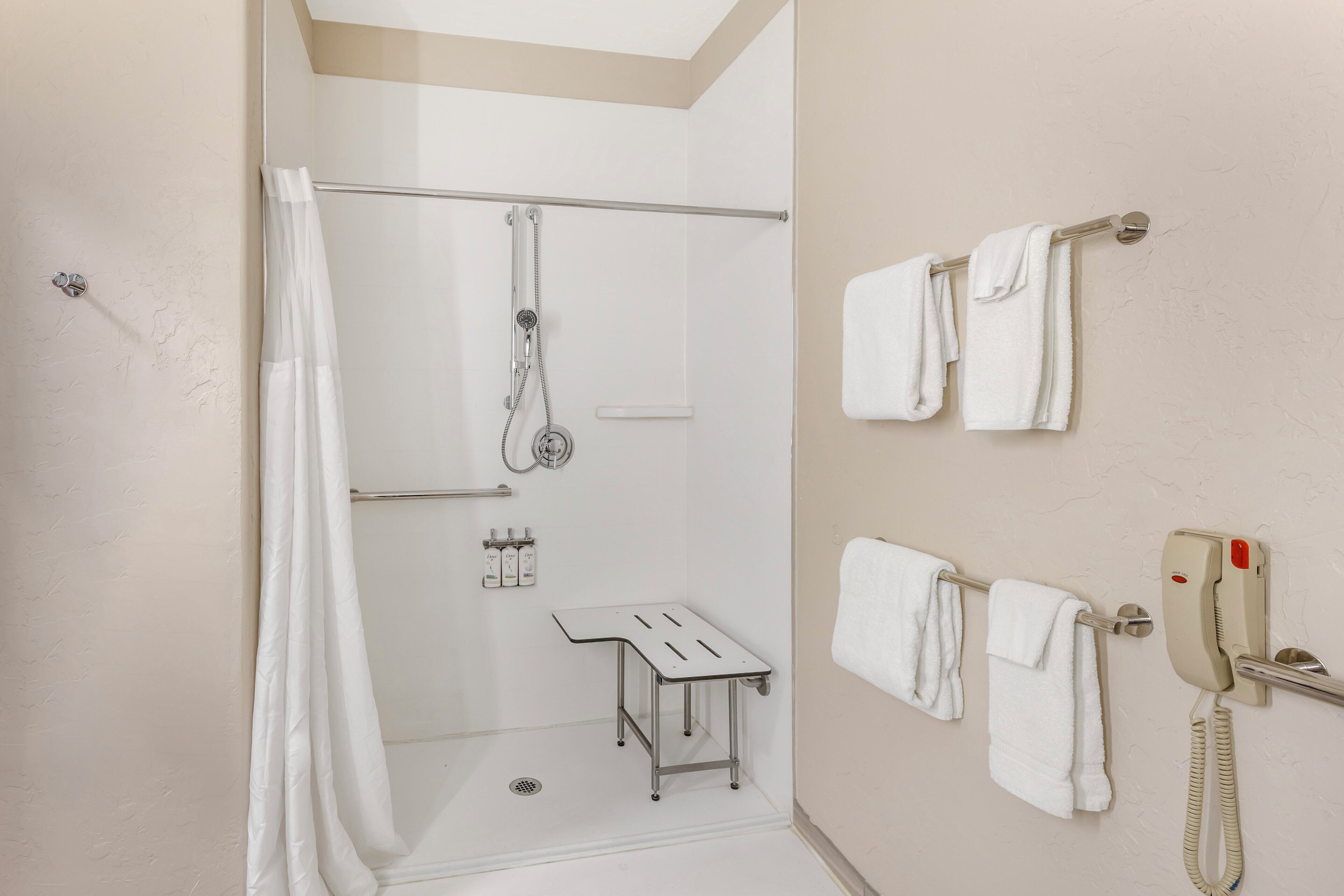 A bathroom with a shower, a towel rack, a small table, and a telephone.