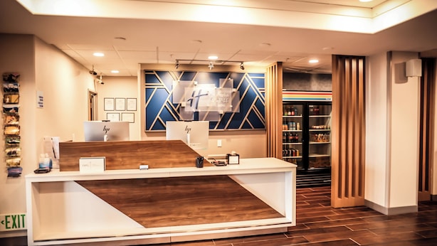 A reception desk with a wooden front panel, framed certificates on the wall, and a 7-Eleven store in the background. - Holiday Inn Express Hotel & Suites Douglas by IHG (Douglas)