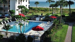 A pool area with lounge chairs and umbrellas, a building with a tiled roof, and a view of the ocean.
